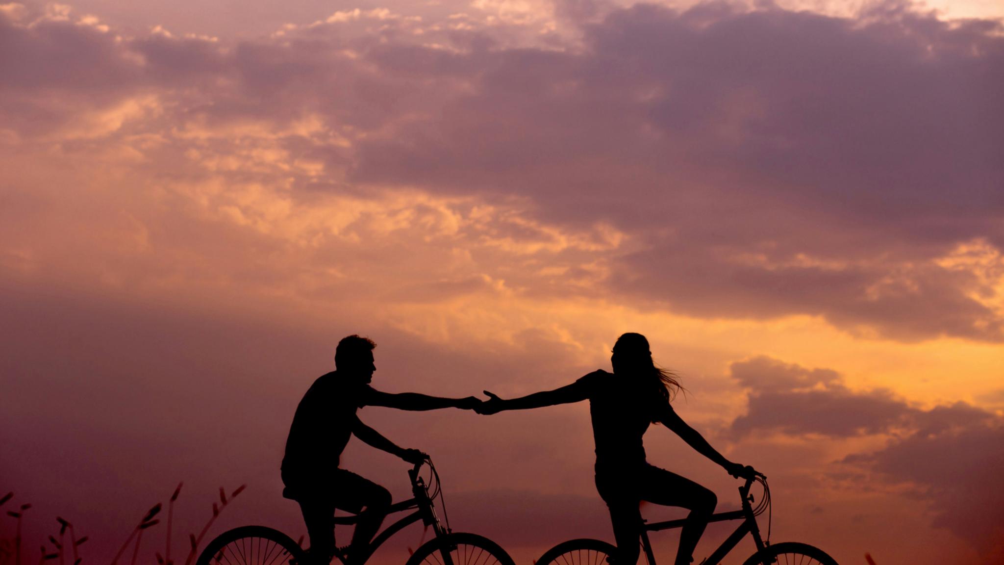 Ein Paar fährt Fahrrad im Sonnenuntergang und reicht sich die Hände