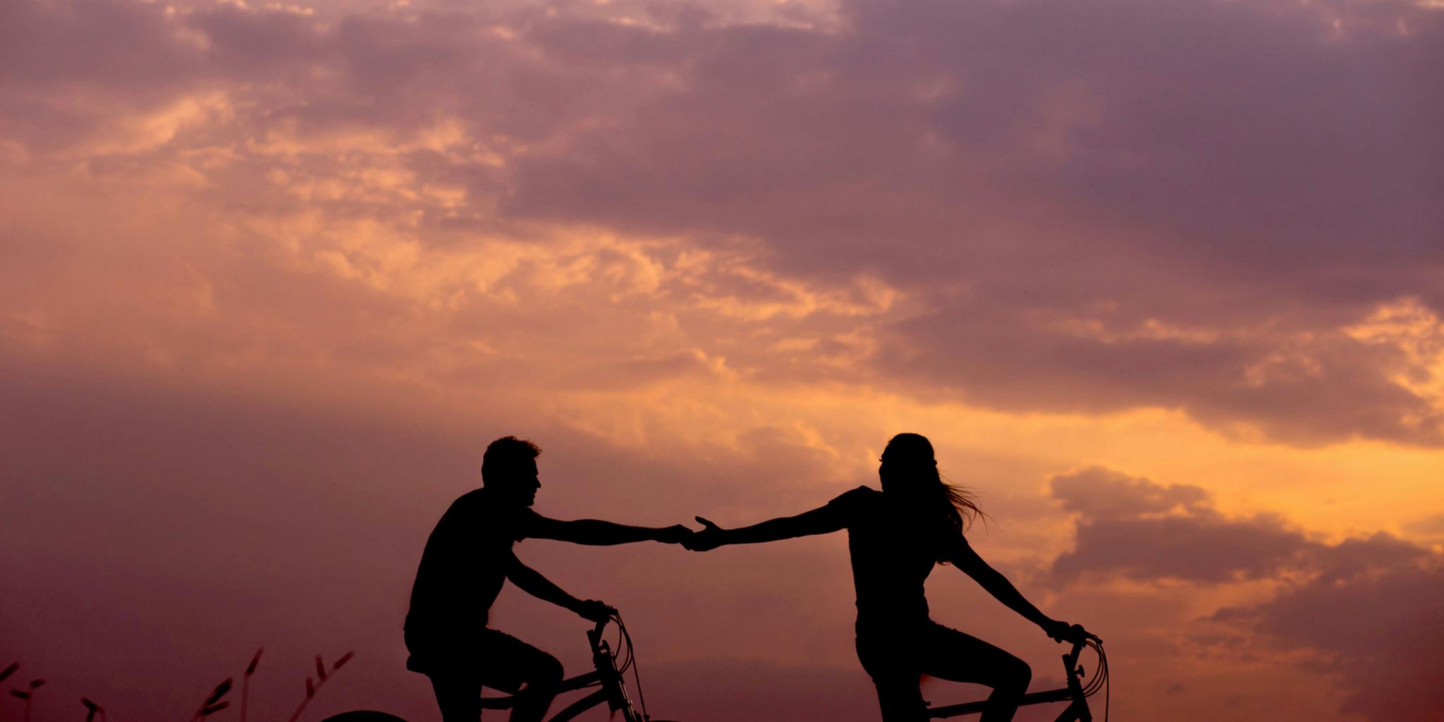 Ein Paar fährt Fahrrad im Sonnenuntergang und reicht sich die Hände (c) Everton Vila / unsplash.com Ein Paar fährt Fahrrad im Sonnenuntergang und reicht sich die Hände