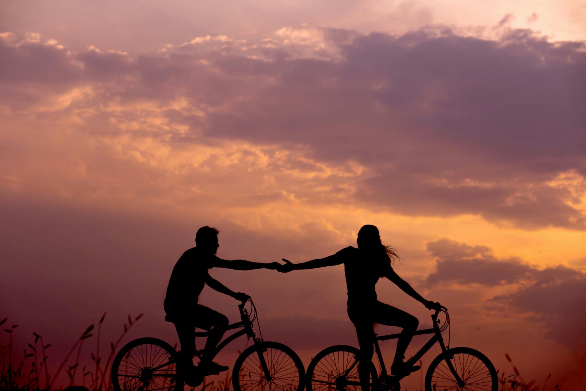 Ein Paar fährt Fahrrad im Sonnenuntergang und reicht sich die Hände