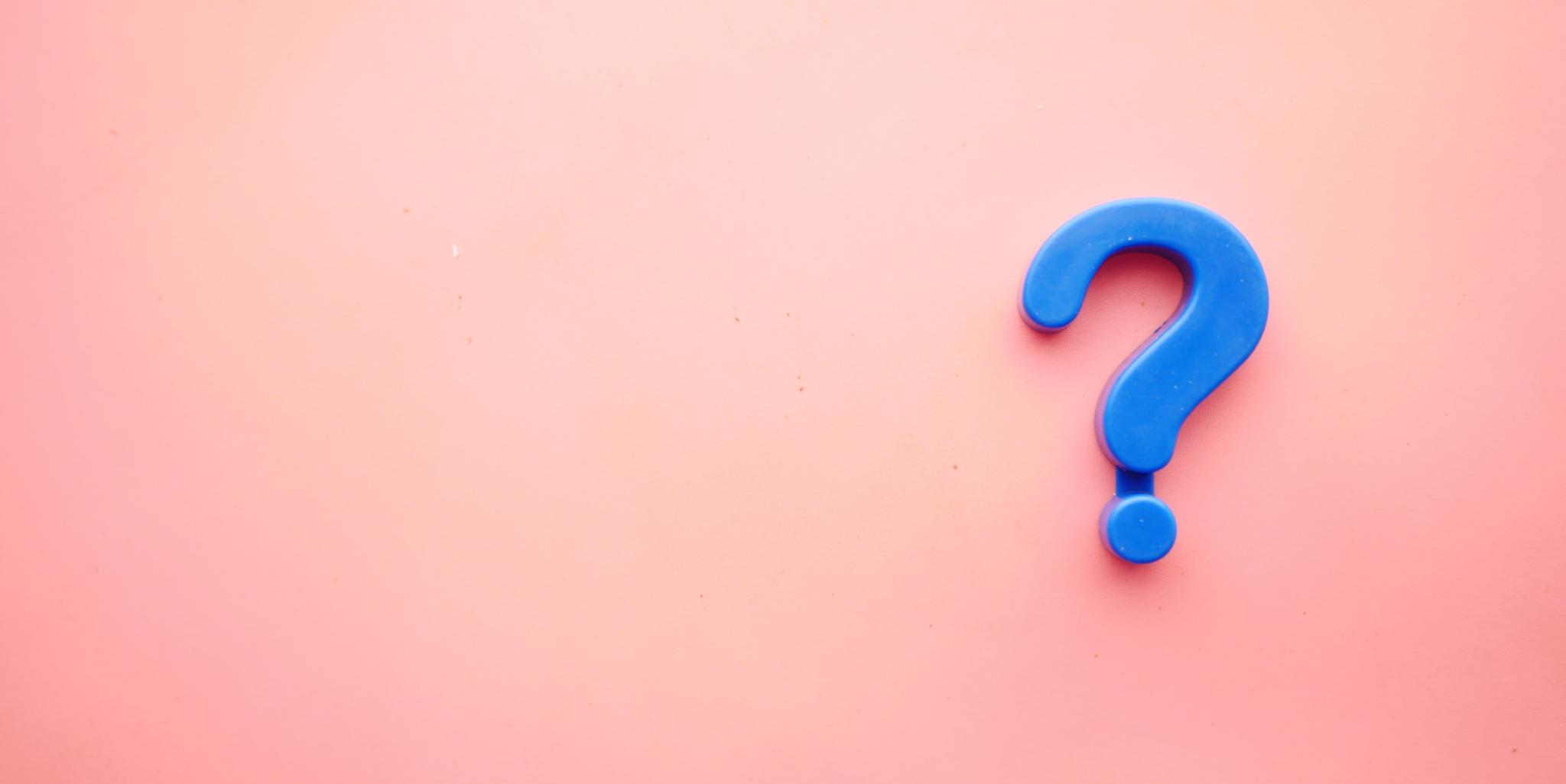 Man sieht ein blaues Fragezeichen auf einem rosafarbenen Hintergrund liegen