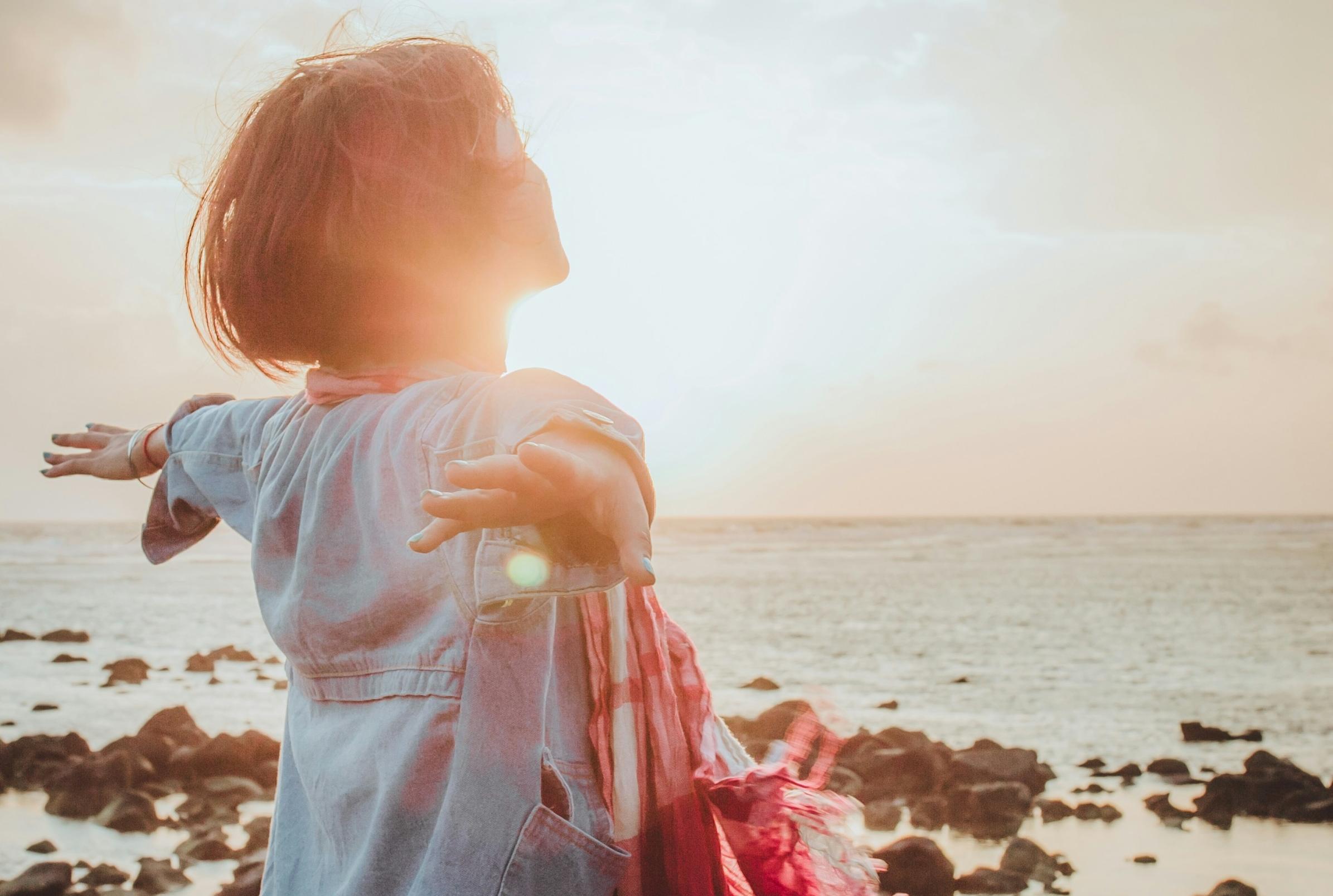 Eine Frau steht im Sonnenuntergang am Strand und breitet die Arme aus