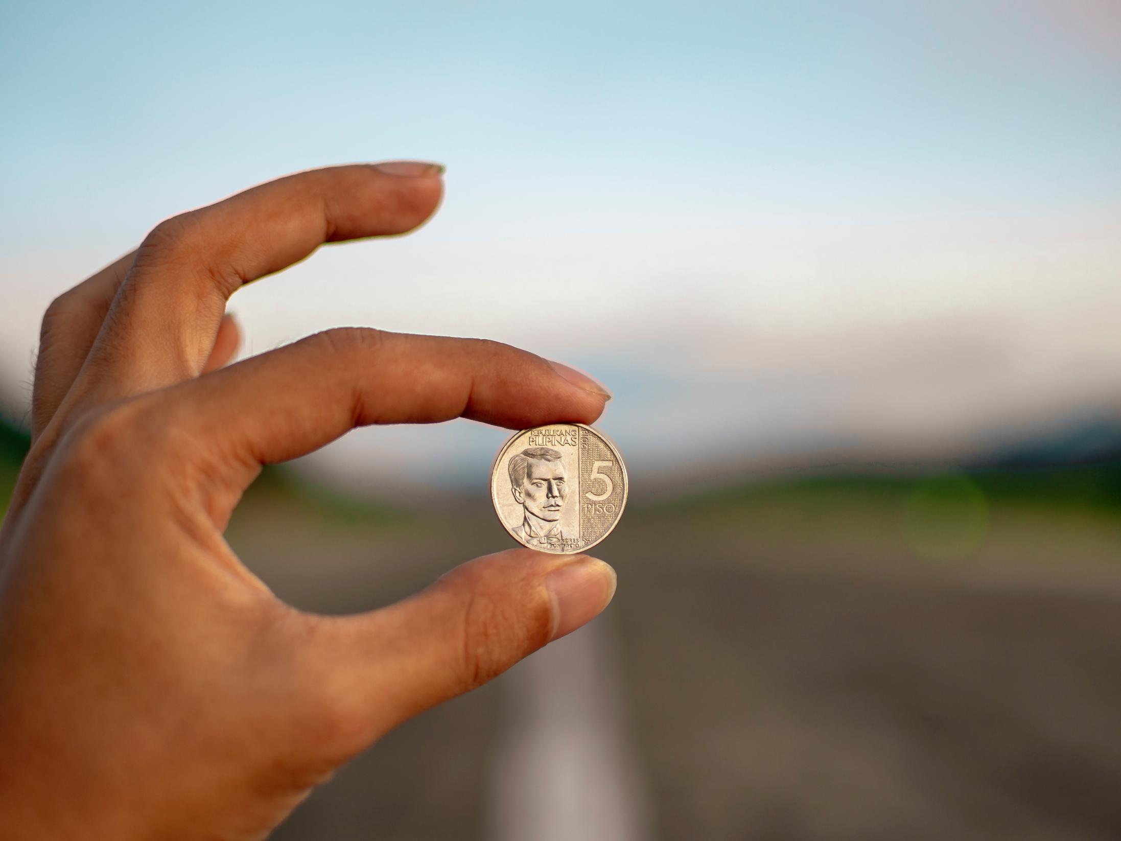 Man sieht eine Hand die zwischen zwei Fingern eine Münze hält