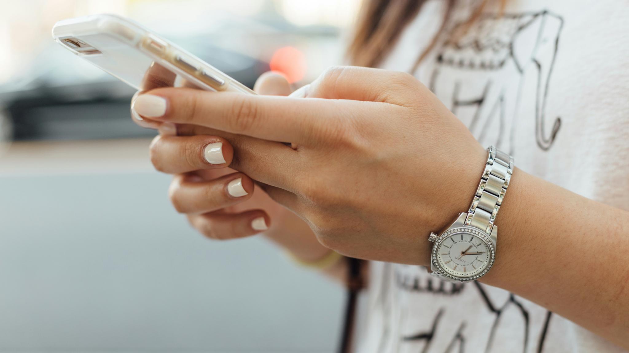 Zwei Hände mit lackierten Nägeln halten ein Handy.