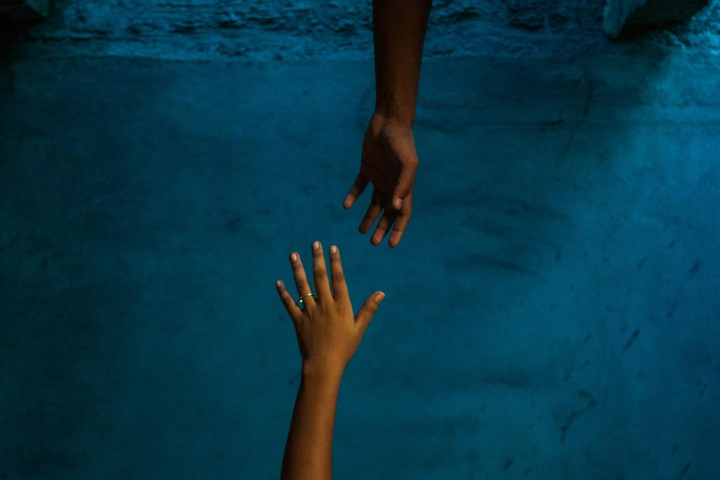 Vor blauem Hintergrund strecken sich zwei Hände einander entgegen.