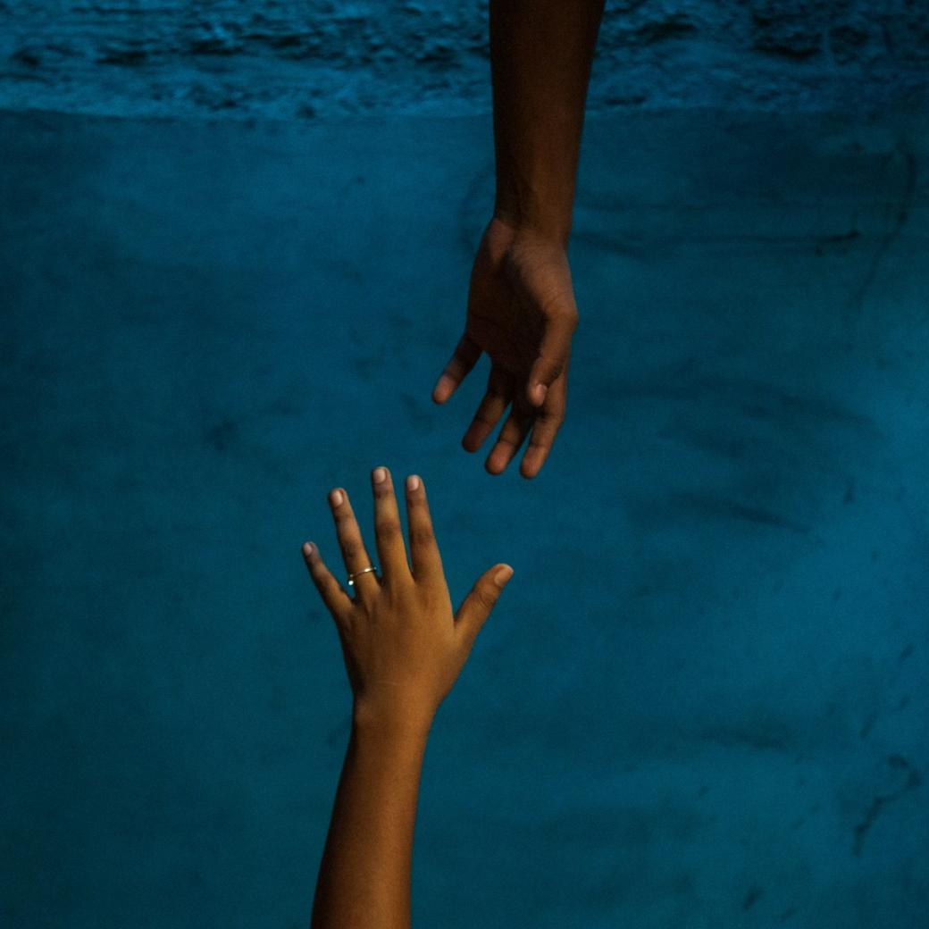 Vor blauem Hintergrund strecken sich zwei Hände einander entgegen.