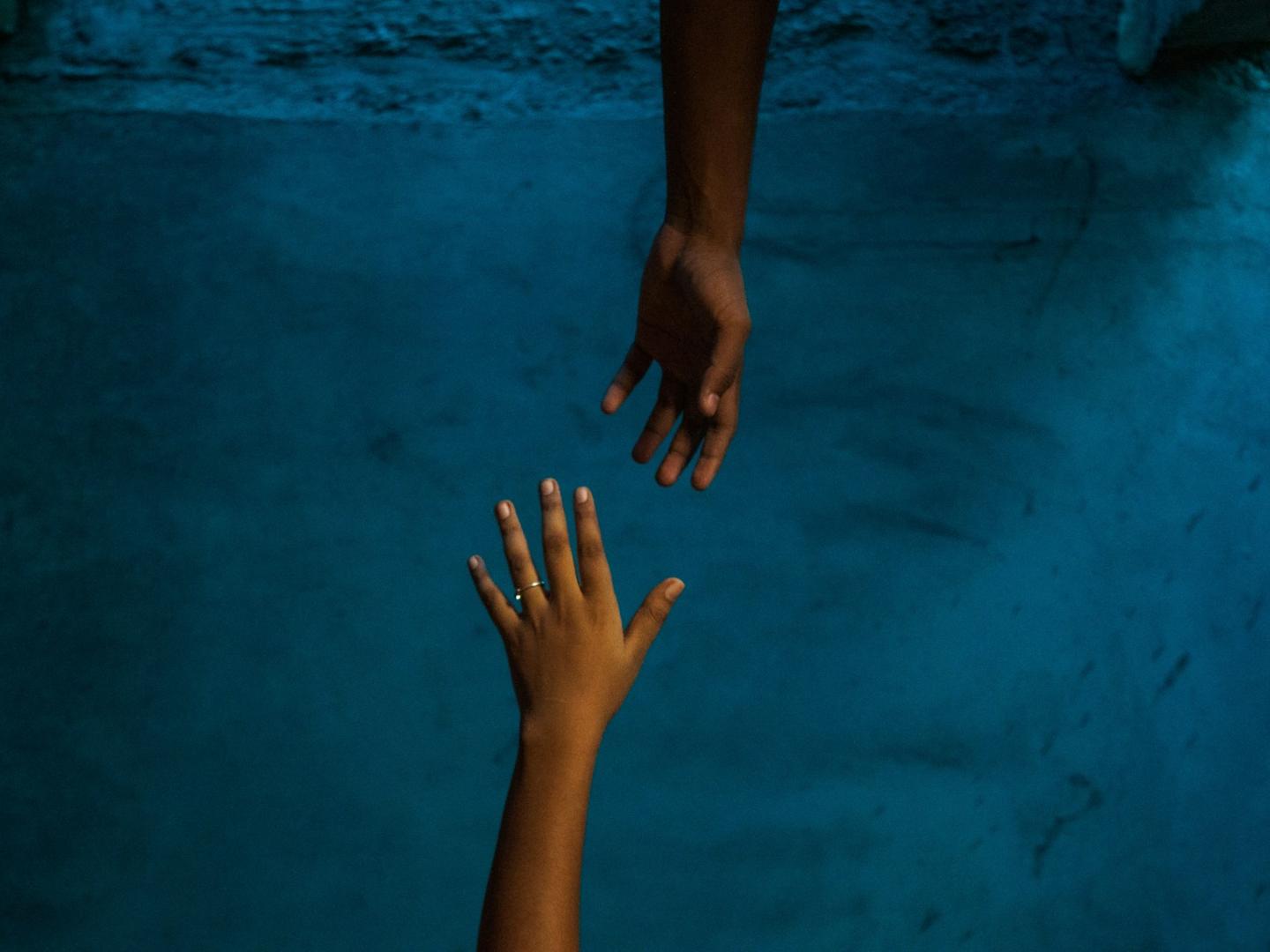 Vor blauem Hintergrund strecken sich zwei Hände einander entgegen.