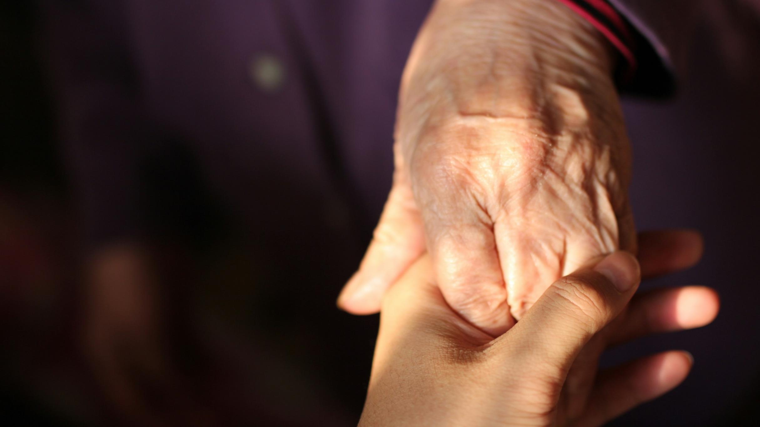 Eine ältere Hand hält eine jüngere Hand.