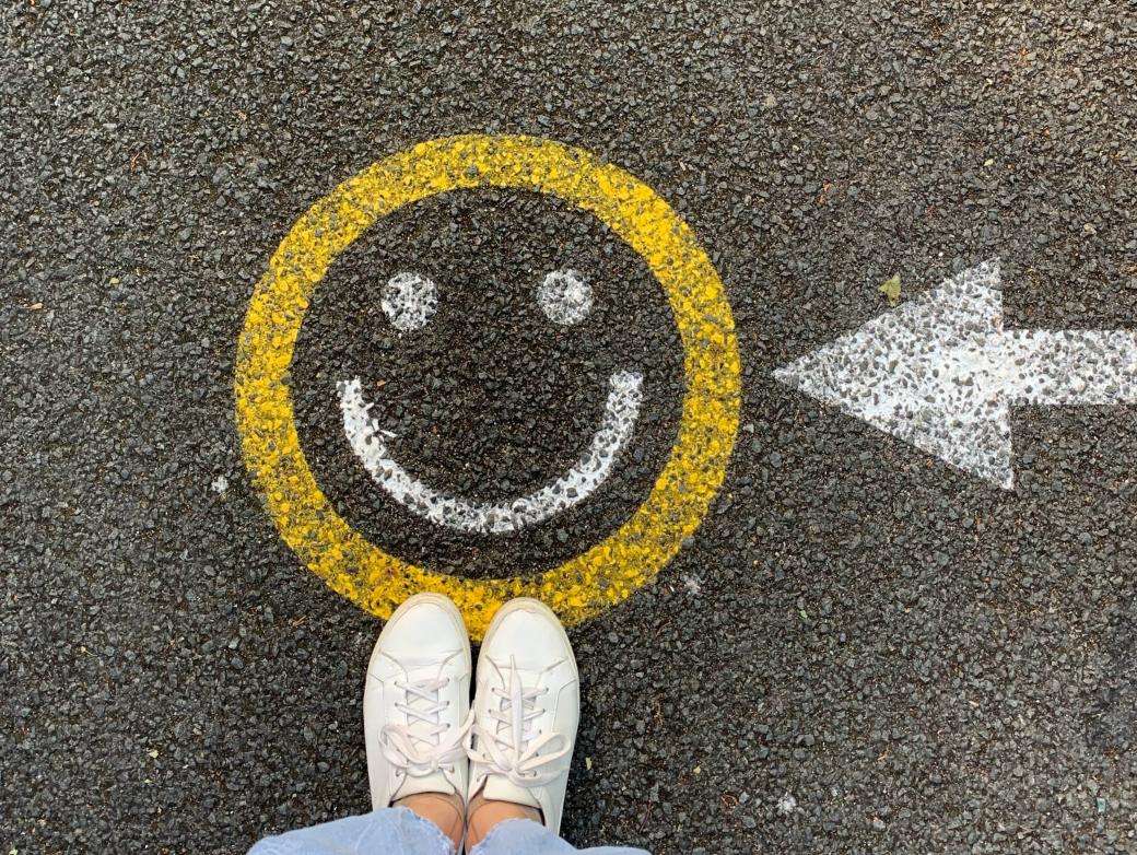 Ein Gesicht ist auf eine Straße aufgemalt. Davor sind zwei Füße mit weißen Stoffschuhen