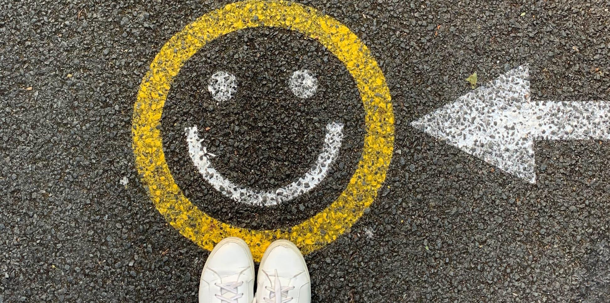 Ein Gesicht ist auf eine Straße aufgemalt. Davor sind zwei Füße mit weißen Stoffschuhen