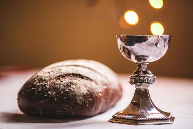 Auf einem Tisch liegt ein Laib Brot und ein silber glänzender Kelch