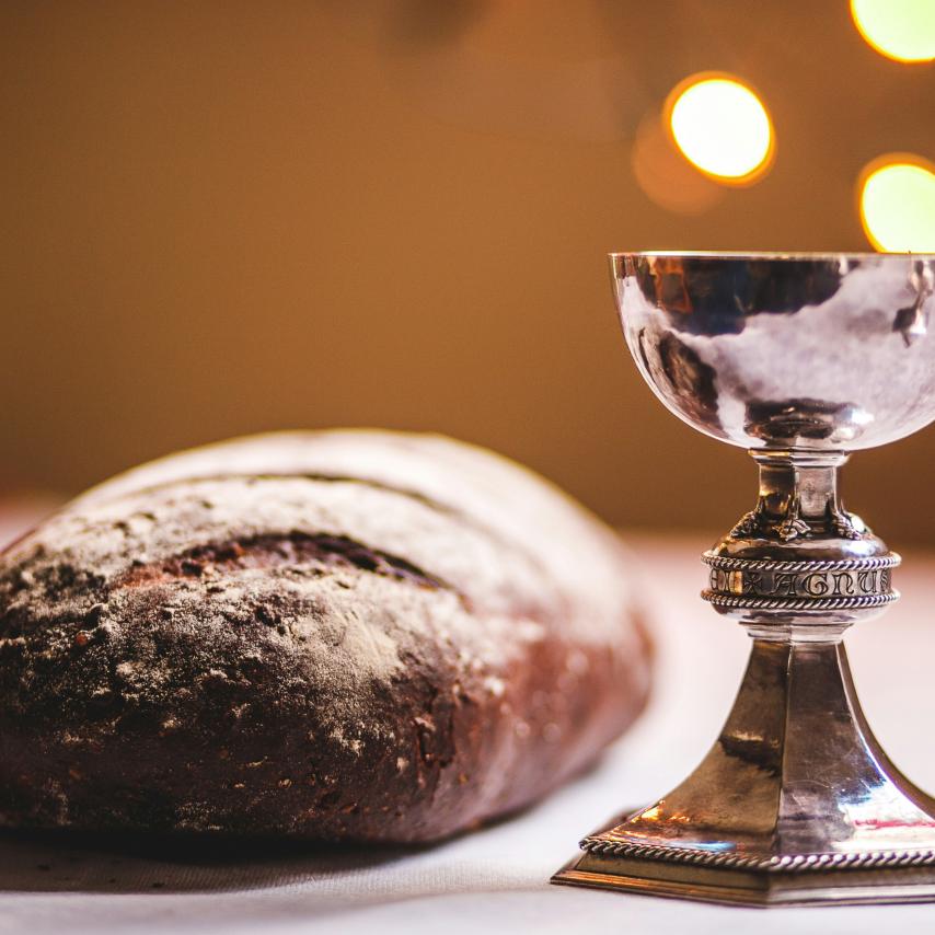 Auf einem Tisch liegt ein Laib Brot und ein silber glänzender Kelch