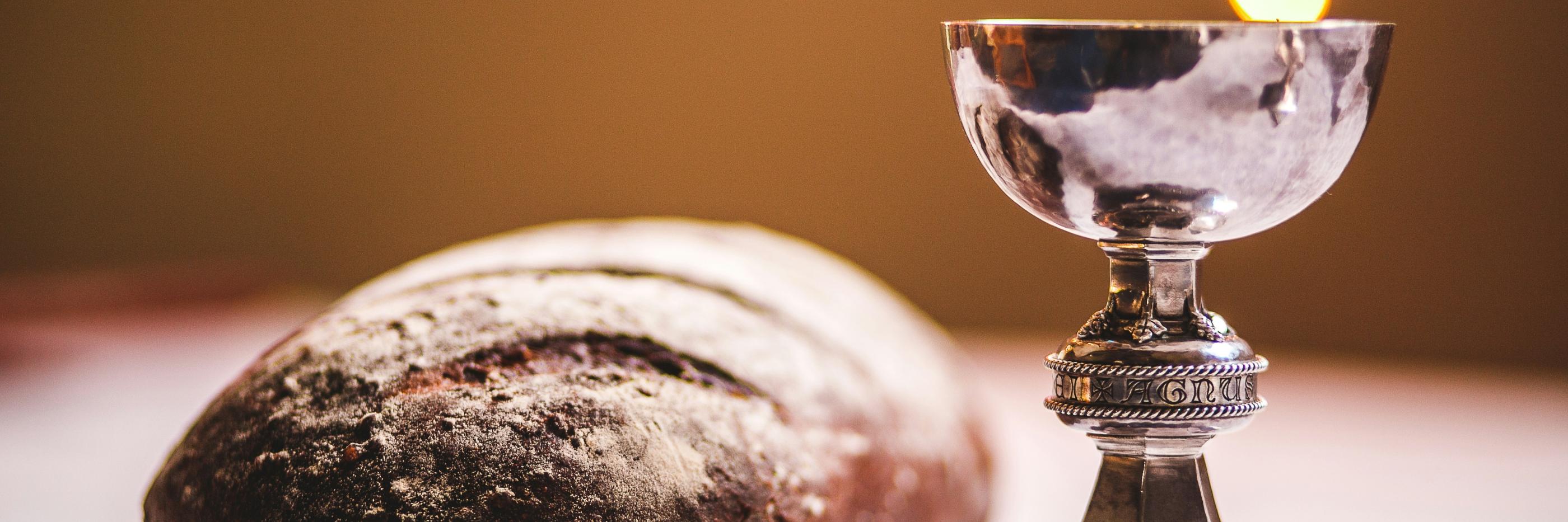 Auf einem Tisch liegt ein Laib Brot und ein silber glänzender Kelch