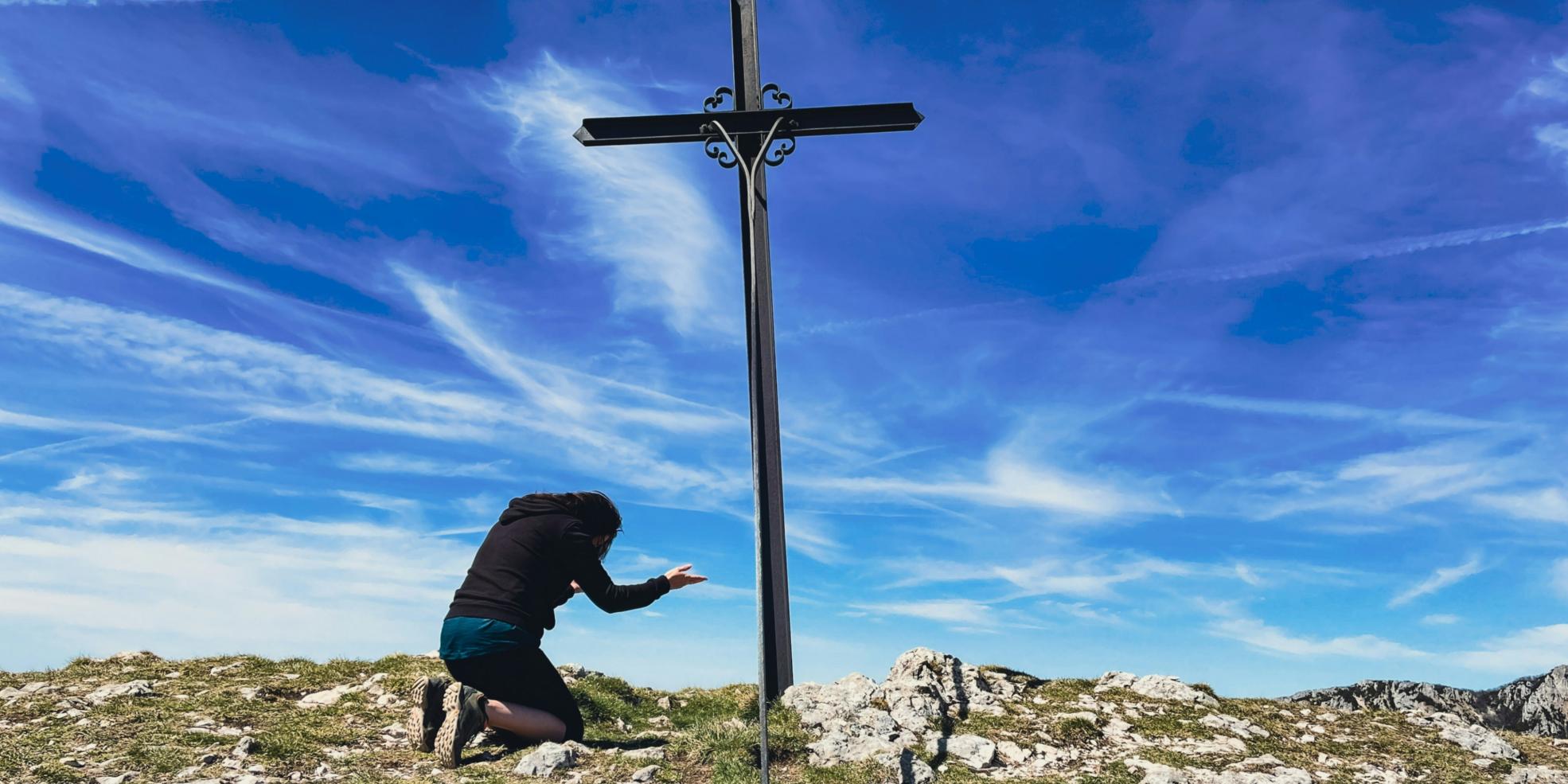 Ein Mann kniet vor einem großen Kreuz auf der Spitze eines Berges.