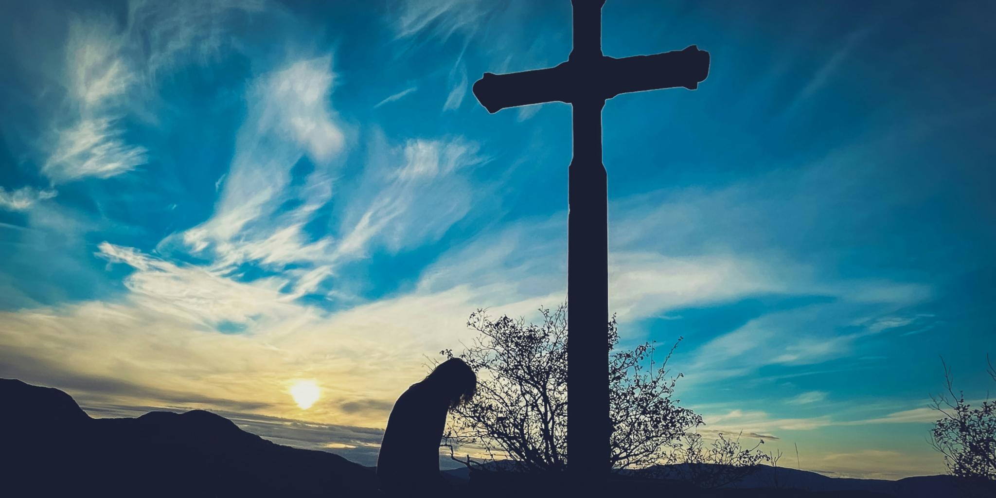 Ein Kreuz steht vor dem Himmel und eine Person verneigt sich davor