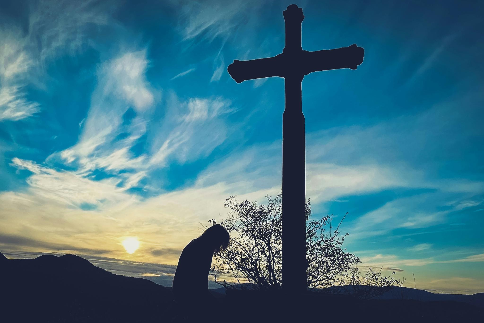 Ein Kreuz steht vor dem Himmel und eine Person verneigt sich davor