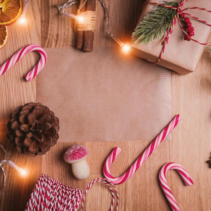 Auf einem Holztisch liegen Zuckerstangen, Packpapier, getrocknete Orangen, Zimtstangen