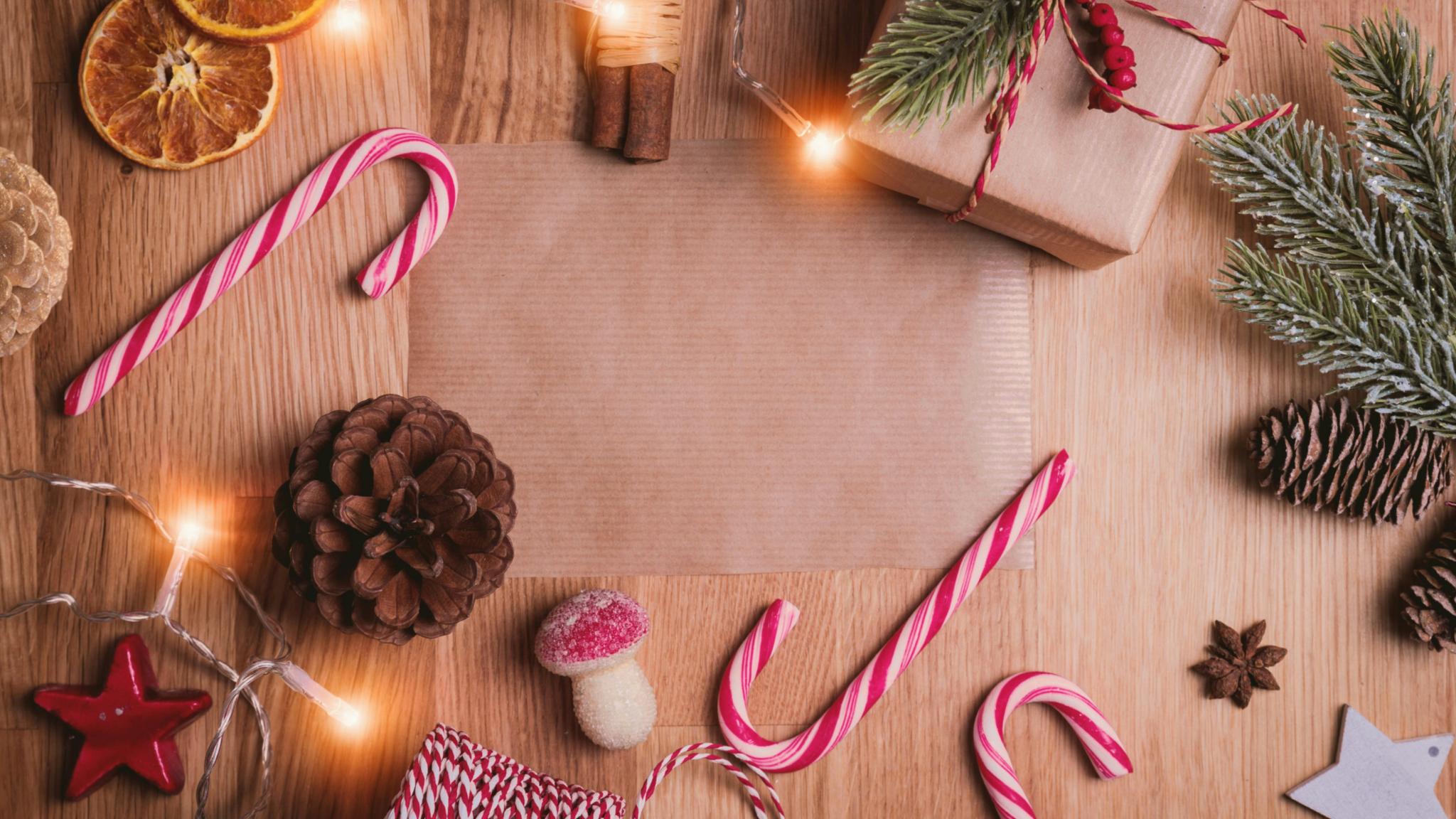 Auf einem Holztisch liegen Zuckerstangen, Packpapier, getrocknete Orangen, Zimtstangen