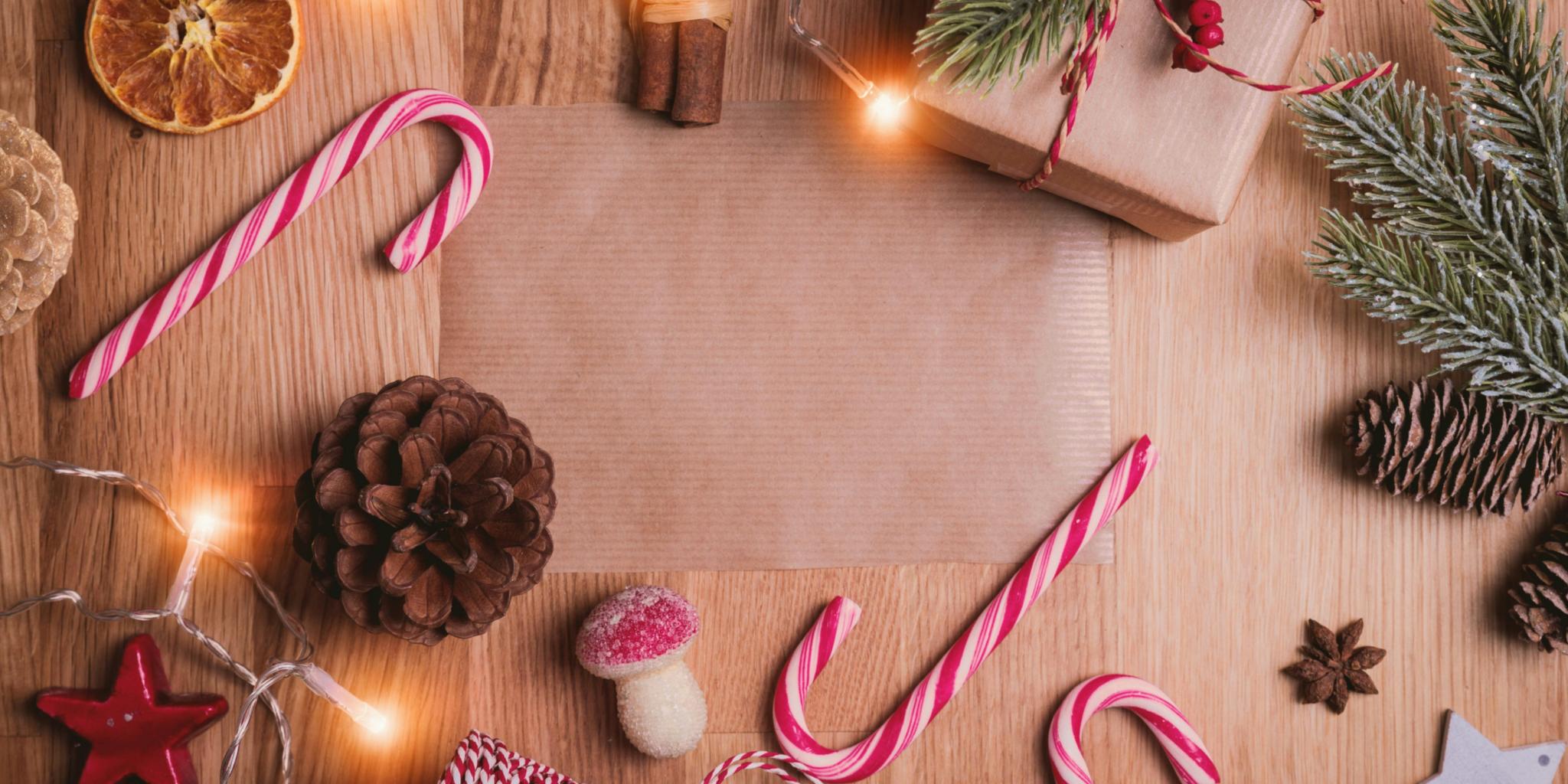 Auf einem Holztisch liegen Zuckerstangen, Packpapier, getrocknete Orangen, Zimtstangen