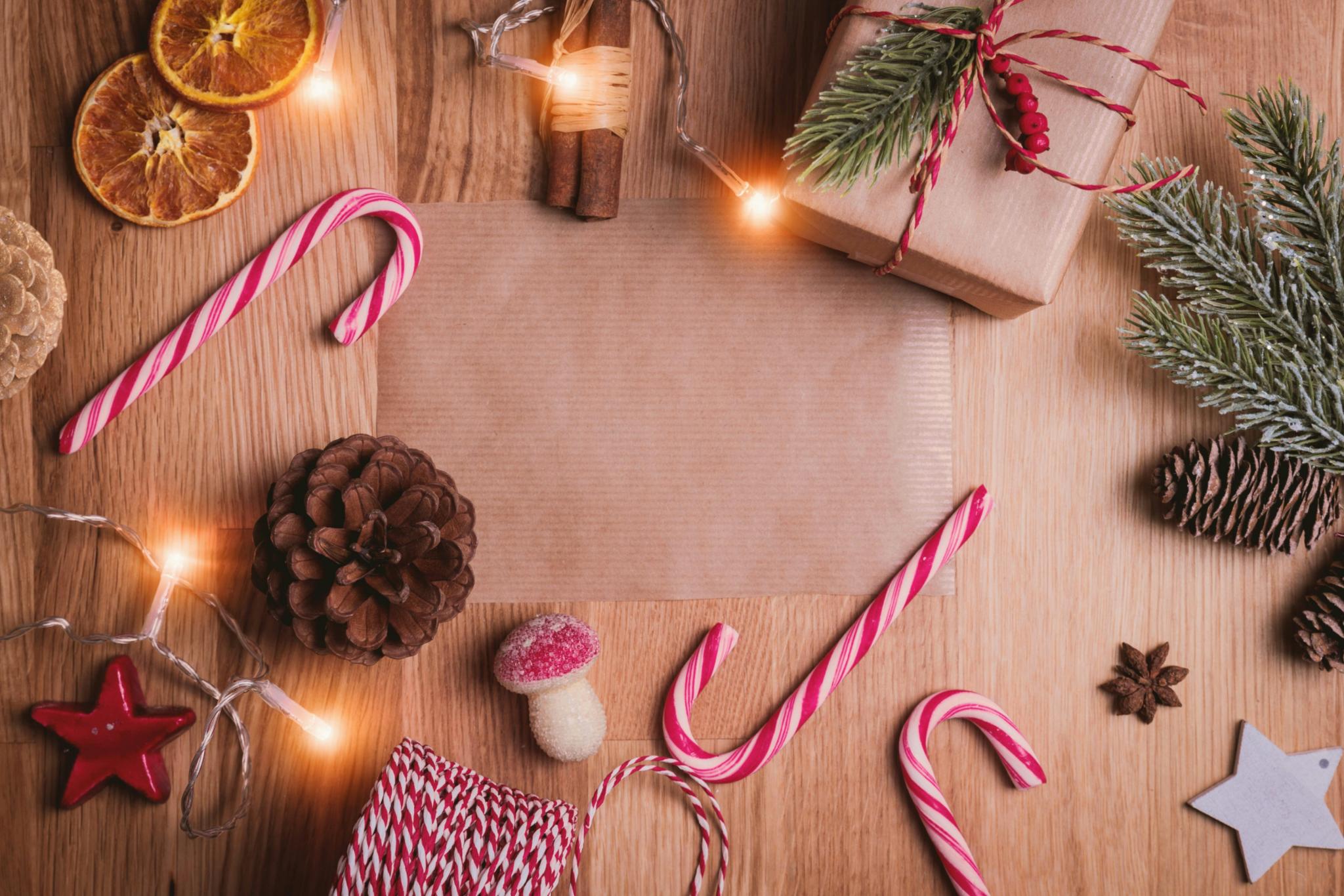 Auf einem Holztisch liegen Zuckerstangen, Packpapier, getrocknete Orangen, Zimtstangen