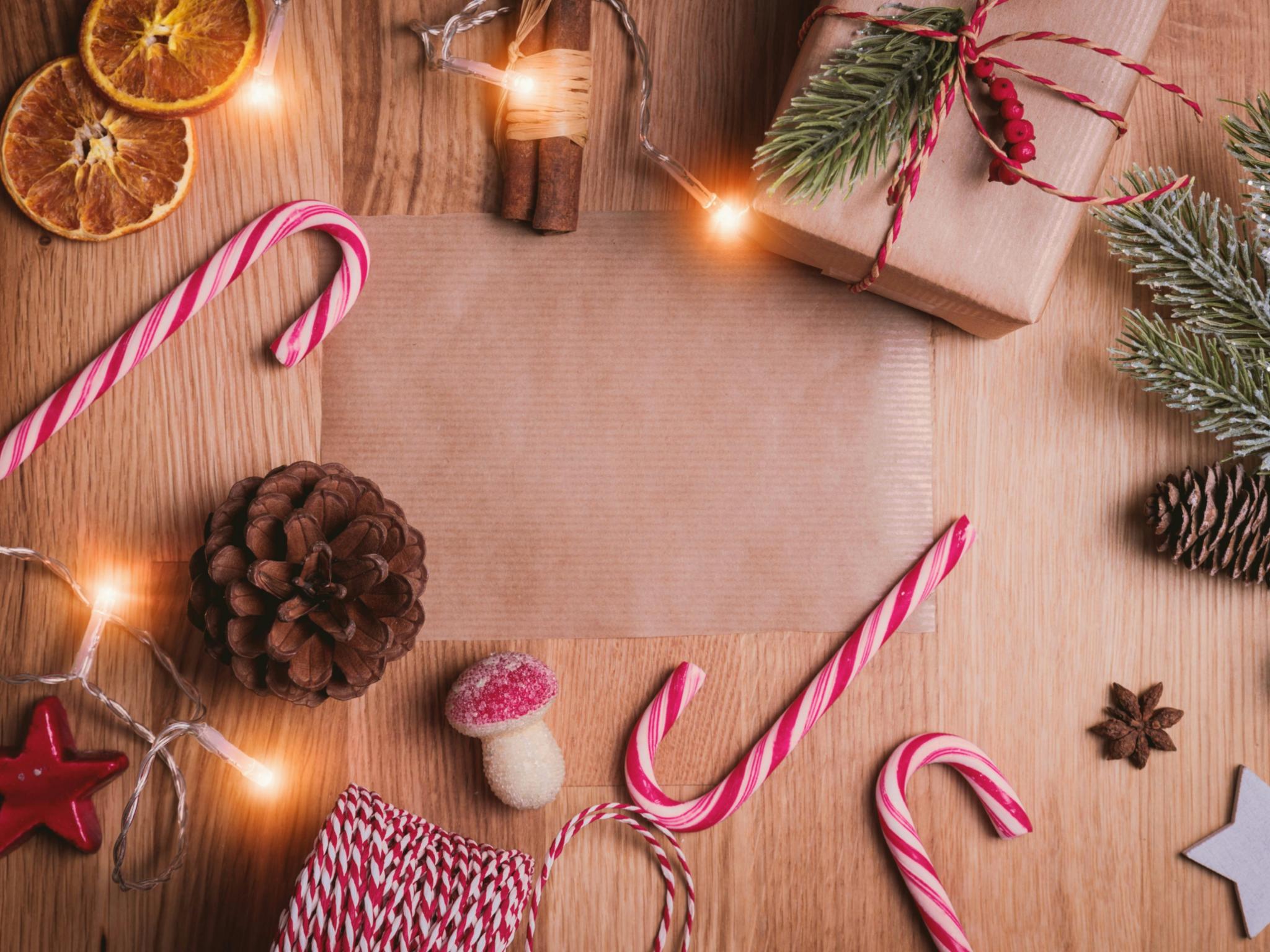Auf einem Holztisch liegen Zuckerstangen, Packpapier, getrocknete Orangen, Zimtstangen