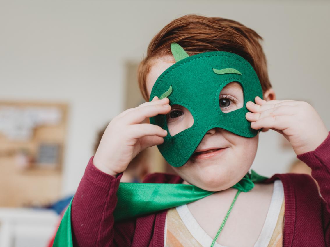lachender kleiner junge mit grüner Superheldenmaske und grünem Umhang