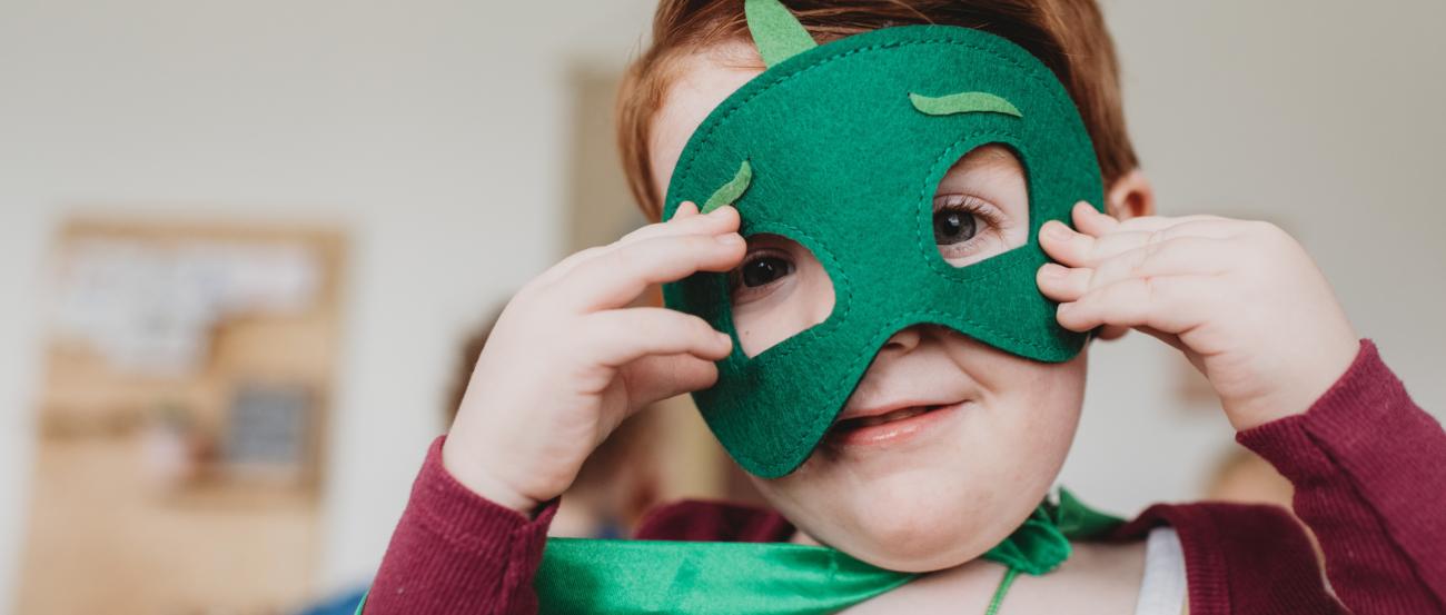 lachender kleiner junge mit grüner Superheldenmaske und grünem Umhang