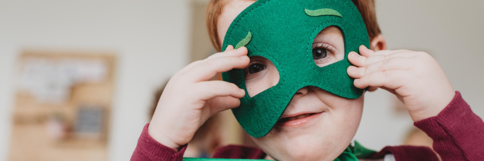 lachender kleiner junge mit grüner Superheldenmaske und grünem Umhang