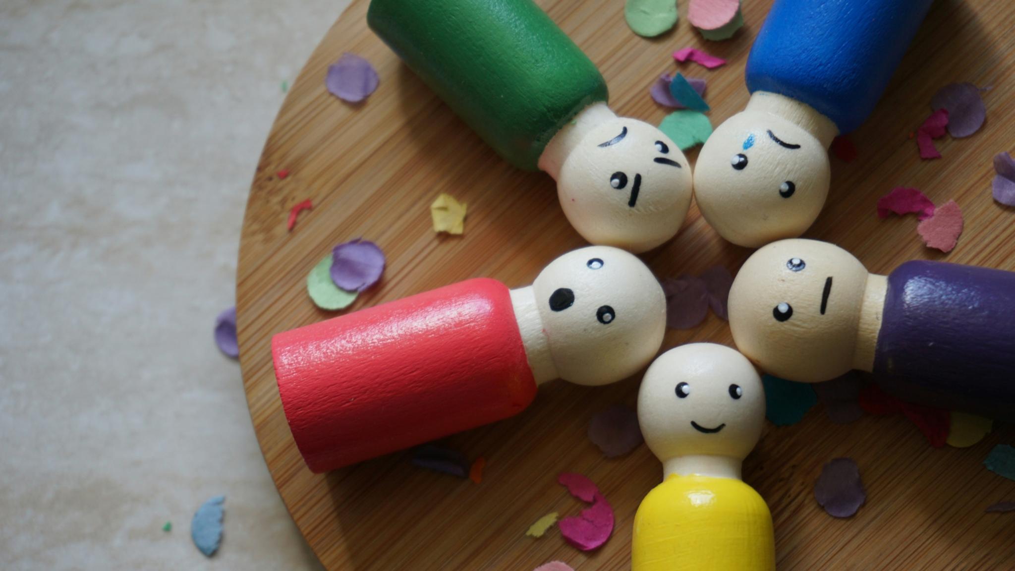 Bunte Figuren aus Holz mit verschiedenen Gesichtsausdrücken liegen auf einem runden Holztablett