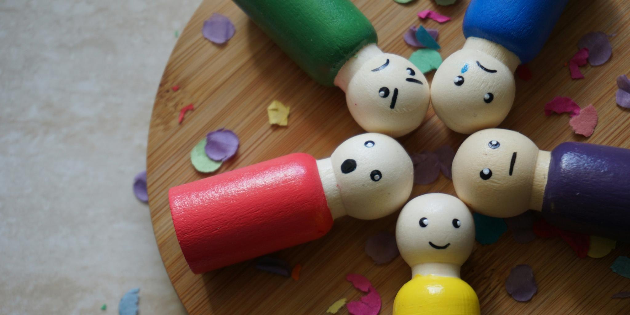 Bunte Figuren aus Holz mit verschiedenen Gesichtsausdrücken liegen auf einem runden Holztablett