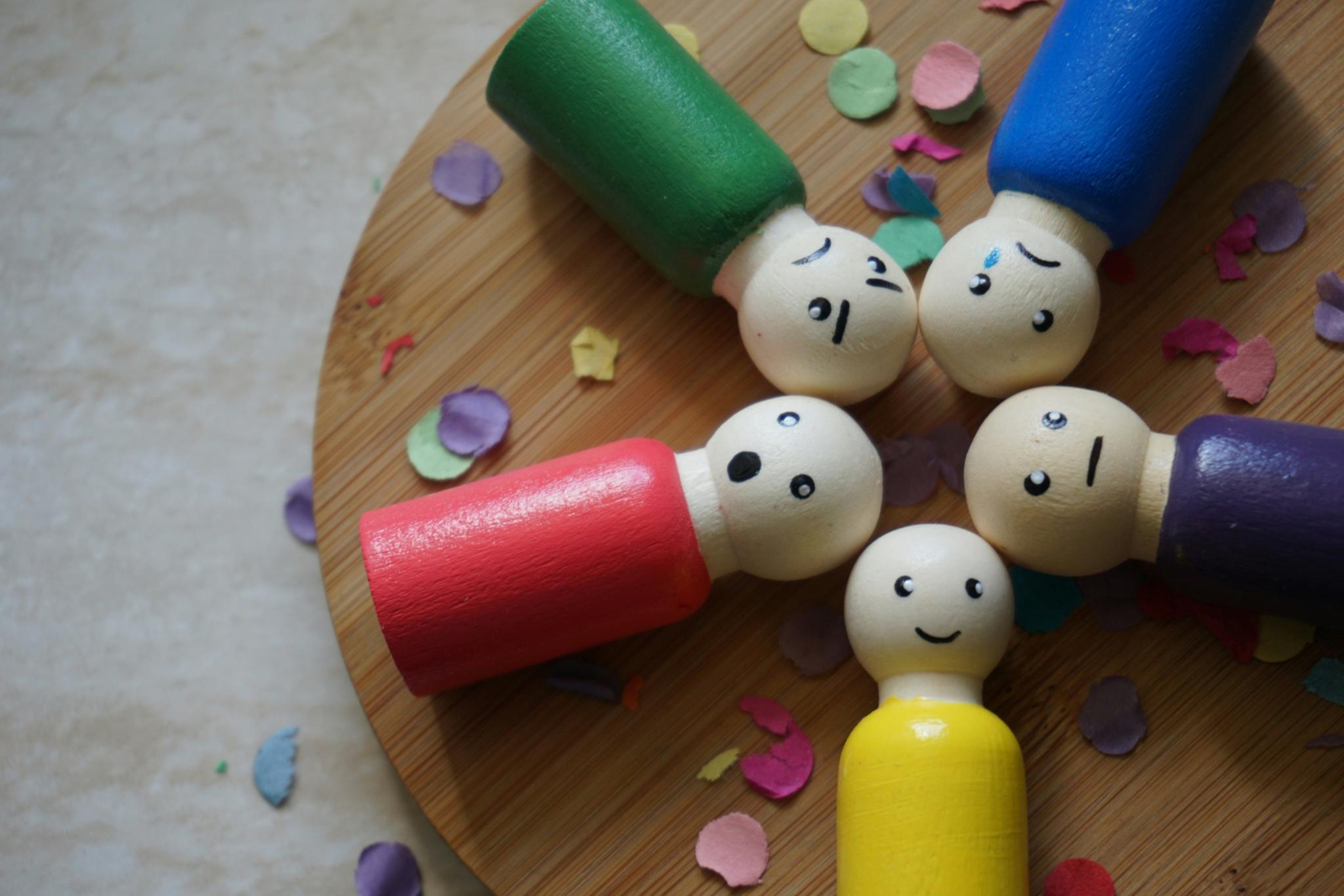 Bunte Figuren aus Holz mit verschiedenen Gesichtsausdrücken liegen auf einem runden Holztablett