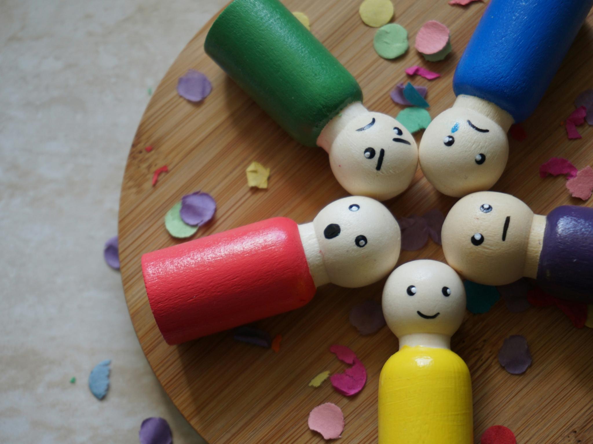 Bunte Figuren aus Holz mit verschiedenen Gesichtsausdrücken liegen auf einem runden Holztablett