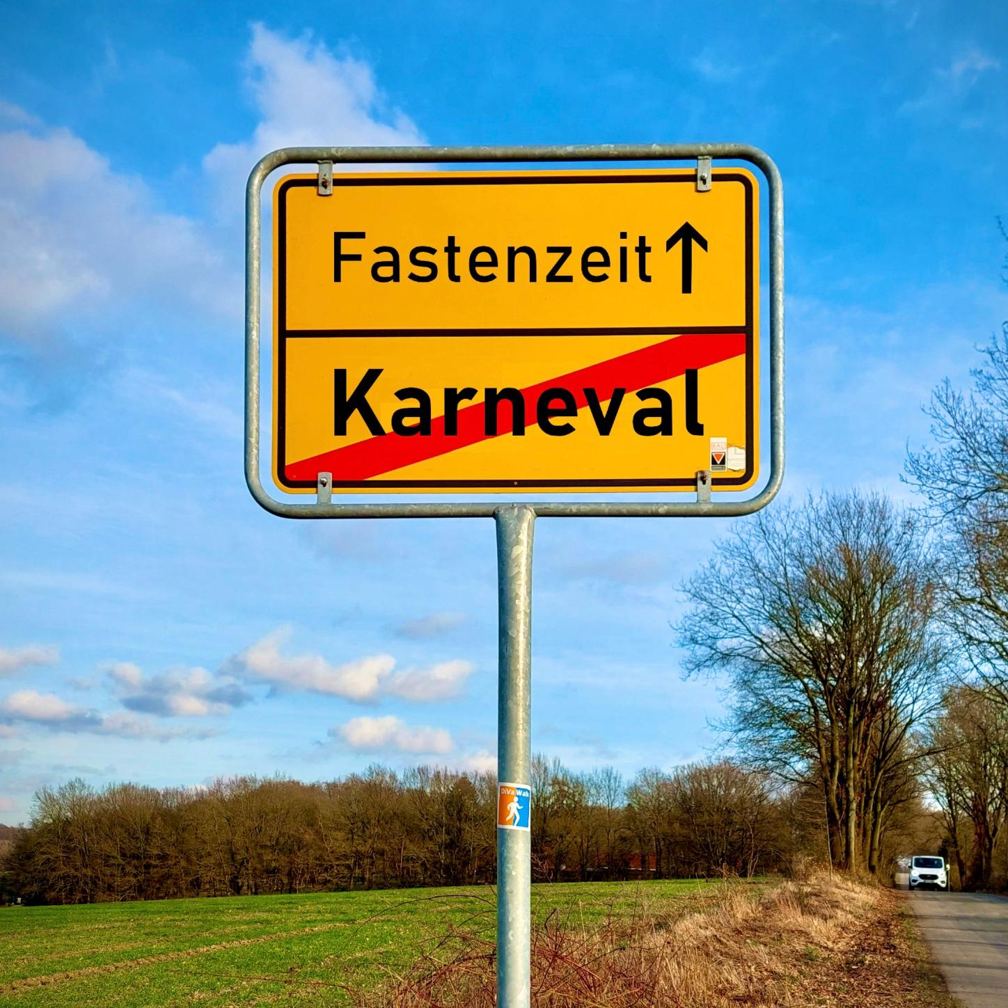 Ein Ortschild in Geld auf dem das Wort Karneval durchgestrichen ist. Darüber steht Fastenzeit mit einem Pfeil der nach vorne weist