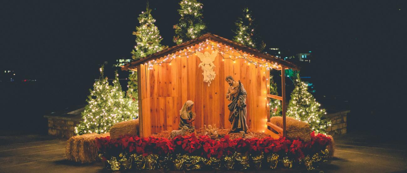 Eine Hütte aus Holz in der Josef und Maria um das Jesuskind stehen. Die Hütte ist beleuchtet, ebenso wie die Bäume im Hintergrund