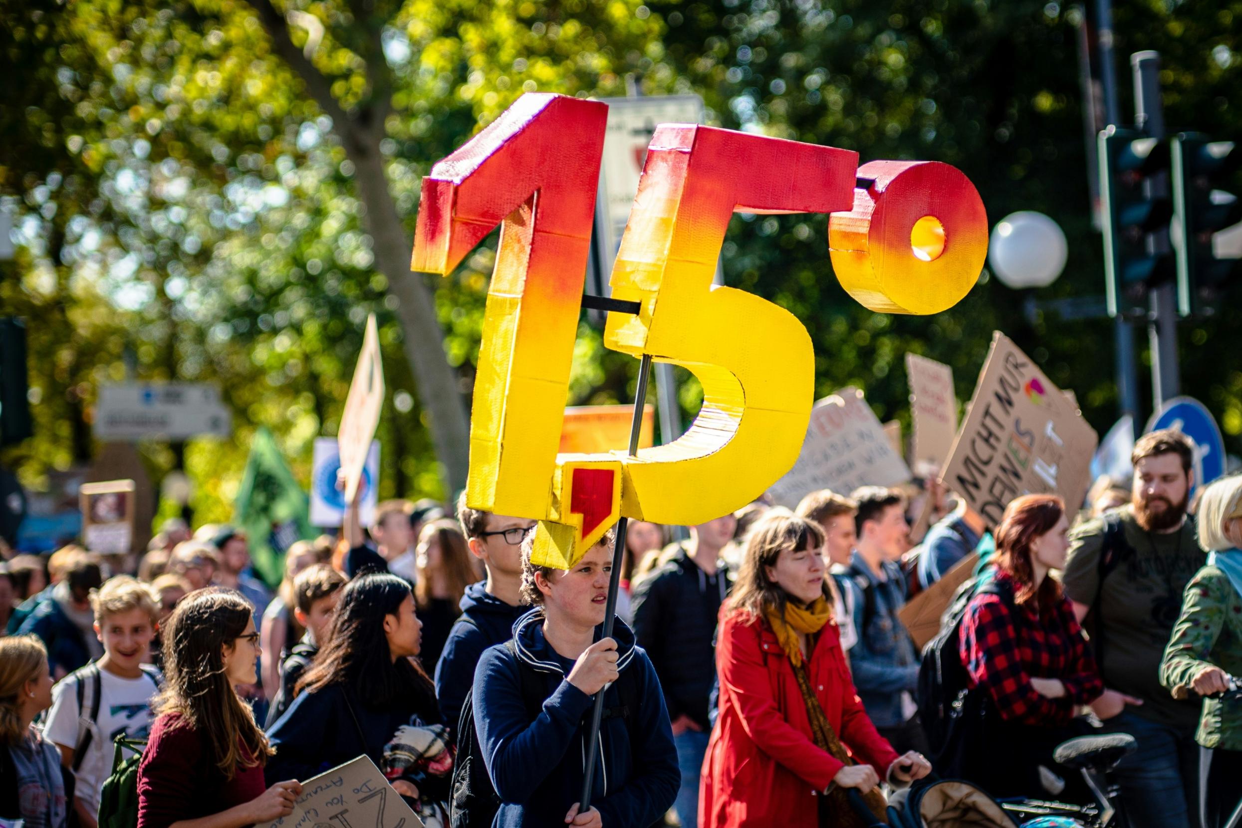 Man sieht eine Gruppe von Demonstrierenden mit Plakaten. Eine Person hält die Zahl '1,5 Grad' aus Pappe in die Luft