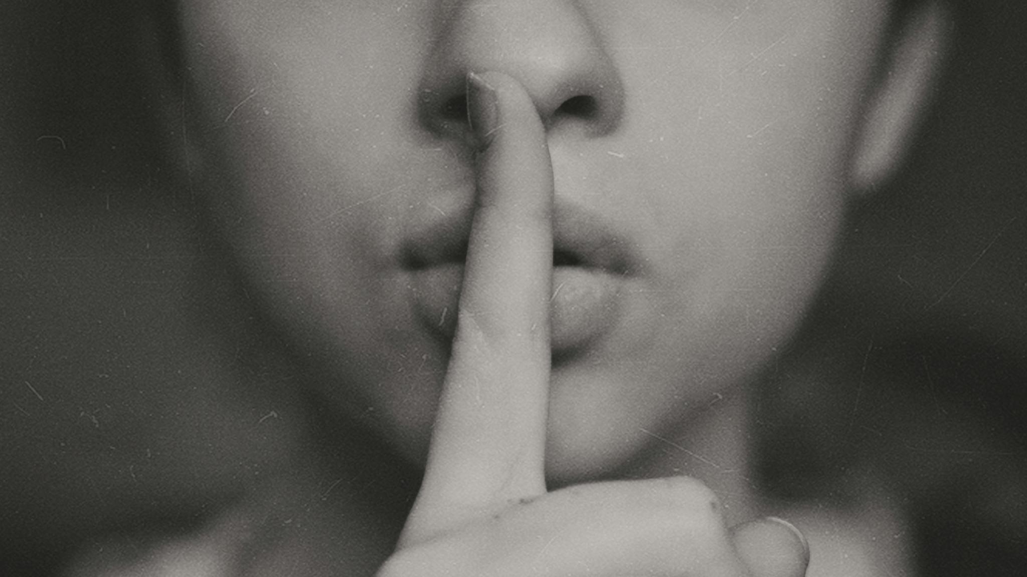 Eine Person hält ihren Zeigefinger vor den Mund um Stille zu signalisieren