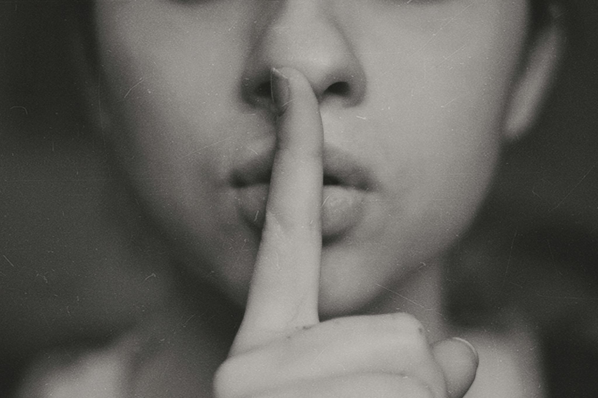 Eine Person hält ihren Zeigefinger vor den Mund um Stille zu signalisieren