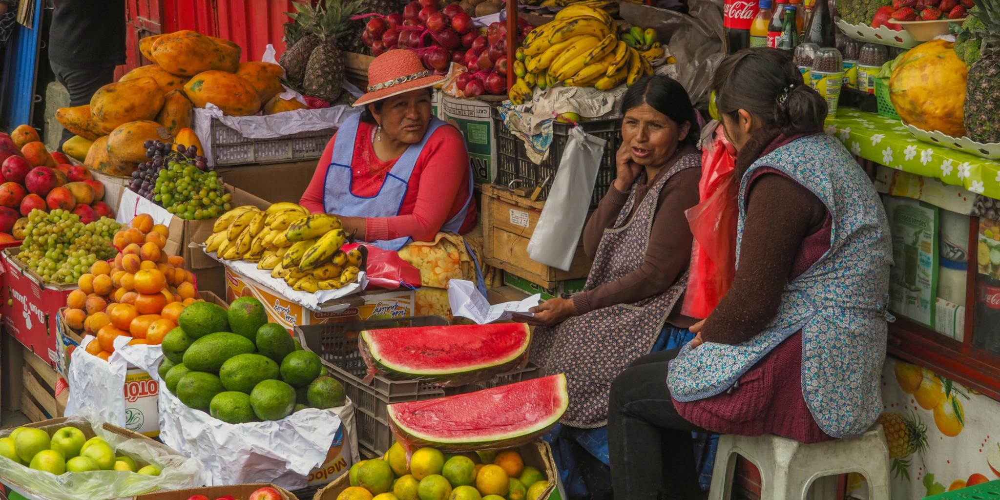 Drei Frauen sitzen inmitten von buntem Obst und Gemüse
