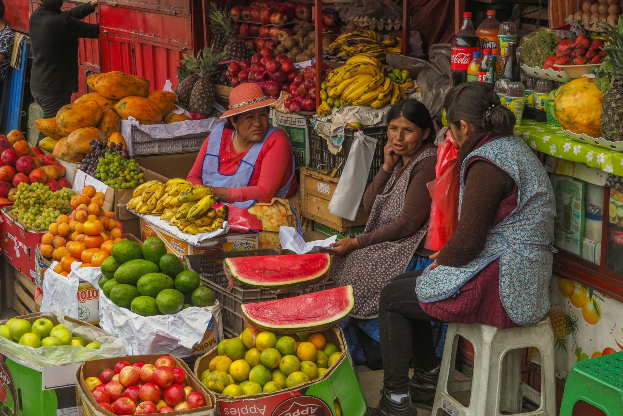 Drei Frauen sitzen inmitten von buntem Obst und Gemüse