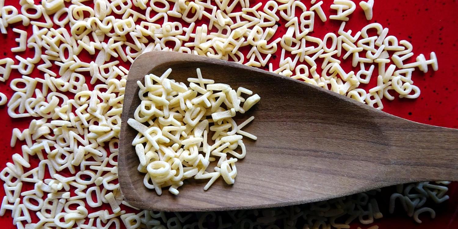 Holzlöffel auf rotem Teller mit Buchstabennudeln