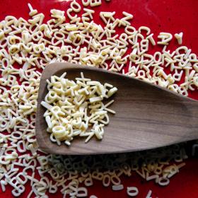 Holzlöffel auf rotem Teller mit Buchstabennudeln