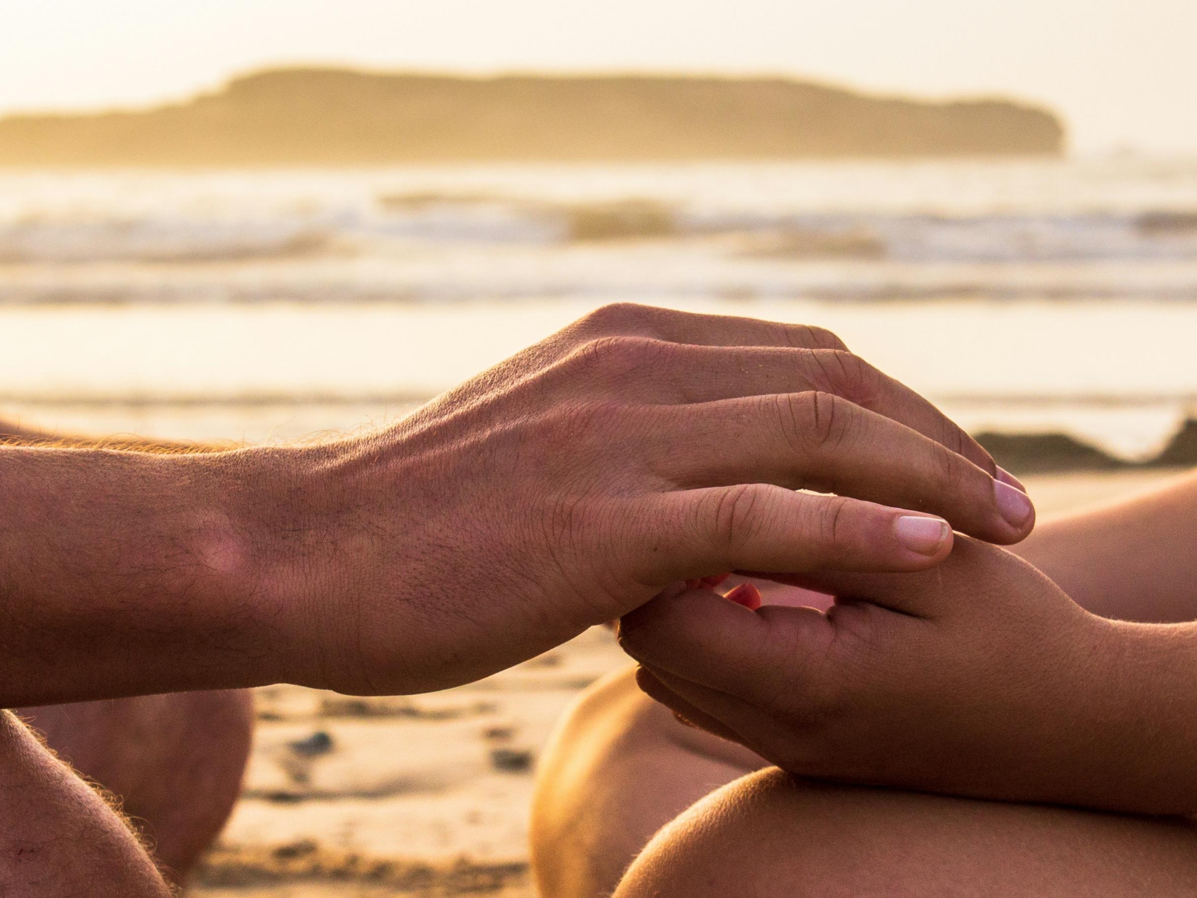 Zwei Hände, die sich halten, im Hintergrund ist das Meer