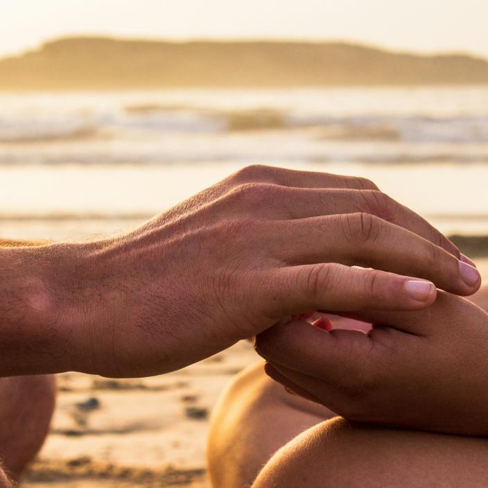 Zwei Hände, die sich halten, im Hintergrund ist das Meer