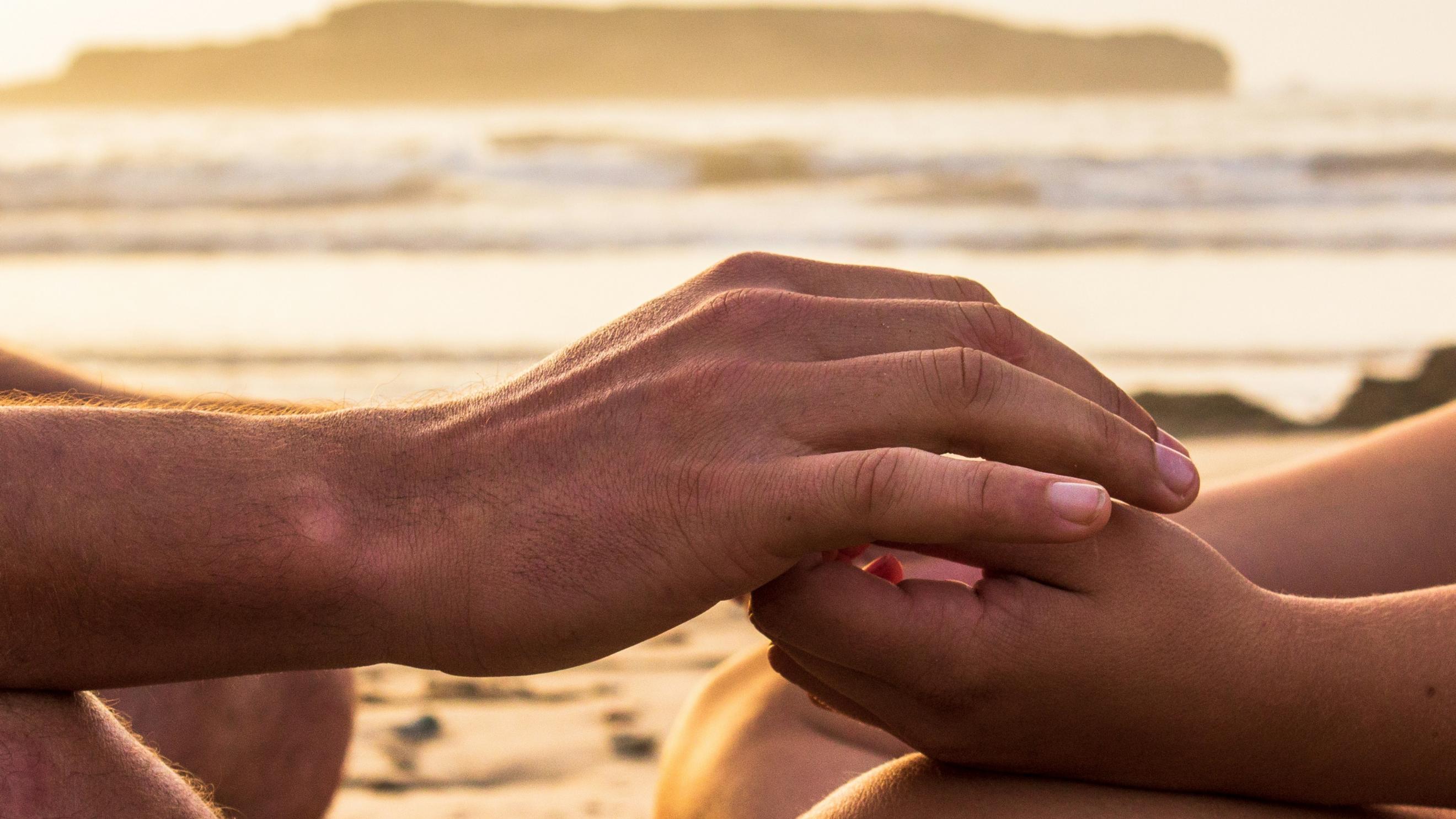 Zwei Hände, die sich halten, im Hintergrund ist das Meer (c) Louis Hansel / unsplash.com Zwei Hände, die sich halten, im Hintergrund ist das Meer
