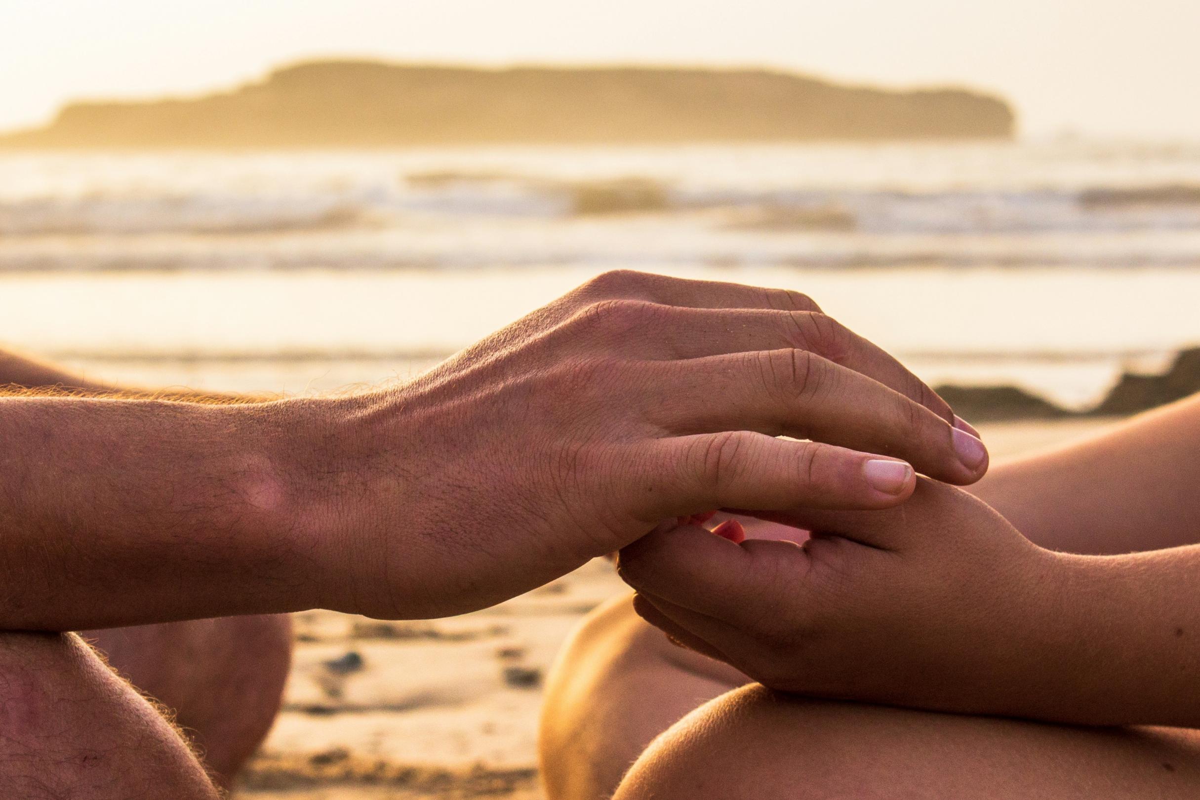 Zwei Hände, die sich halten, im Hintergrund ist das Meer