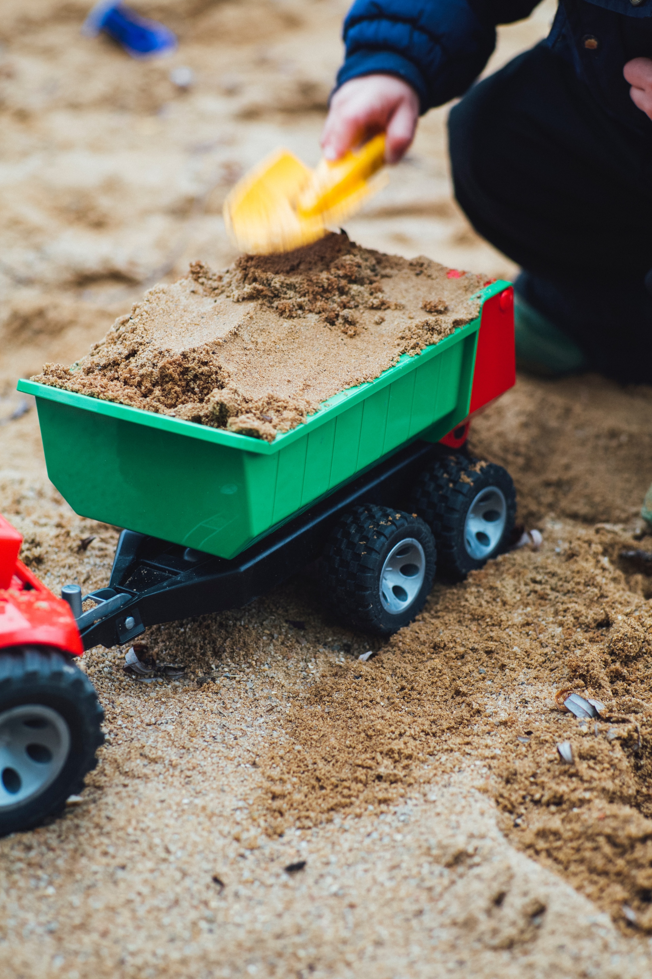 Ein Kind belädt im Sandkasten einen Spielzeuganhänger mit Sand