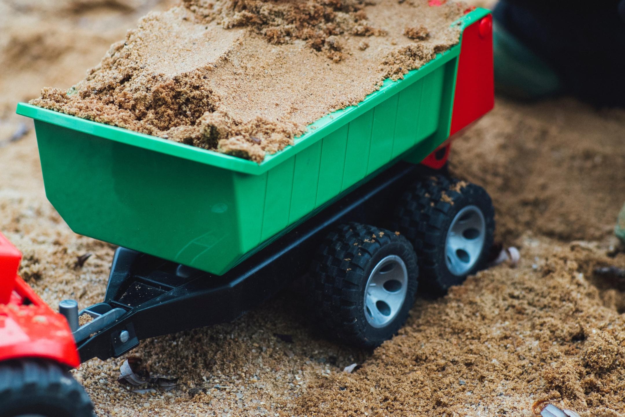 Ein Kind belädt im Sandkasten einen Spielzeuganhänger mit Sand