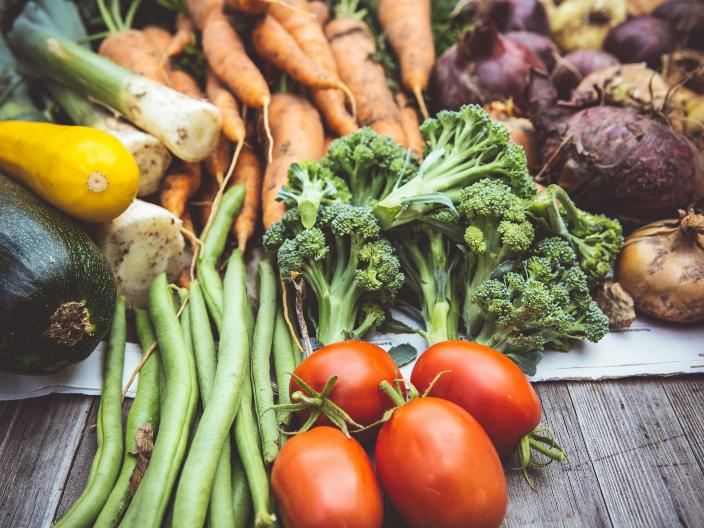 Zucchini, Lauch, Karotten, Zwiebeln, Bohnen, Tomaten und Broccoli liegen auf einem Tisch aus Holz