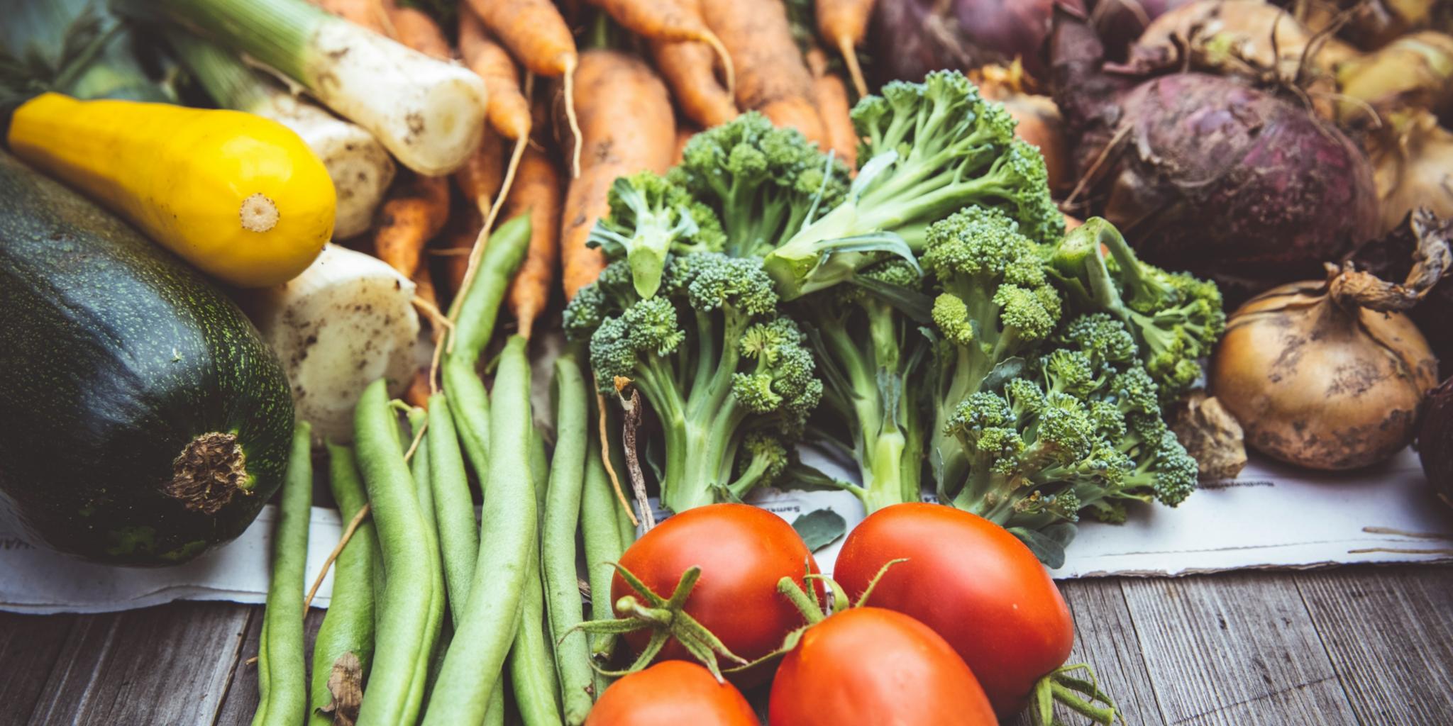 Zucchini, Lauch, Karotten, Zwiebeln, Bohnen, Tomaten und Broccoli liegen auf einem Tisch aus Holz