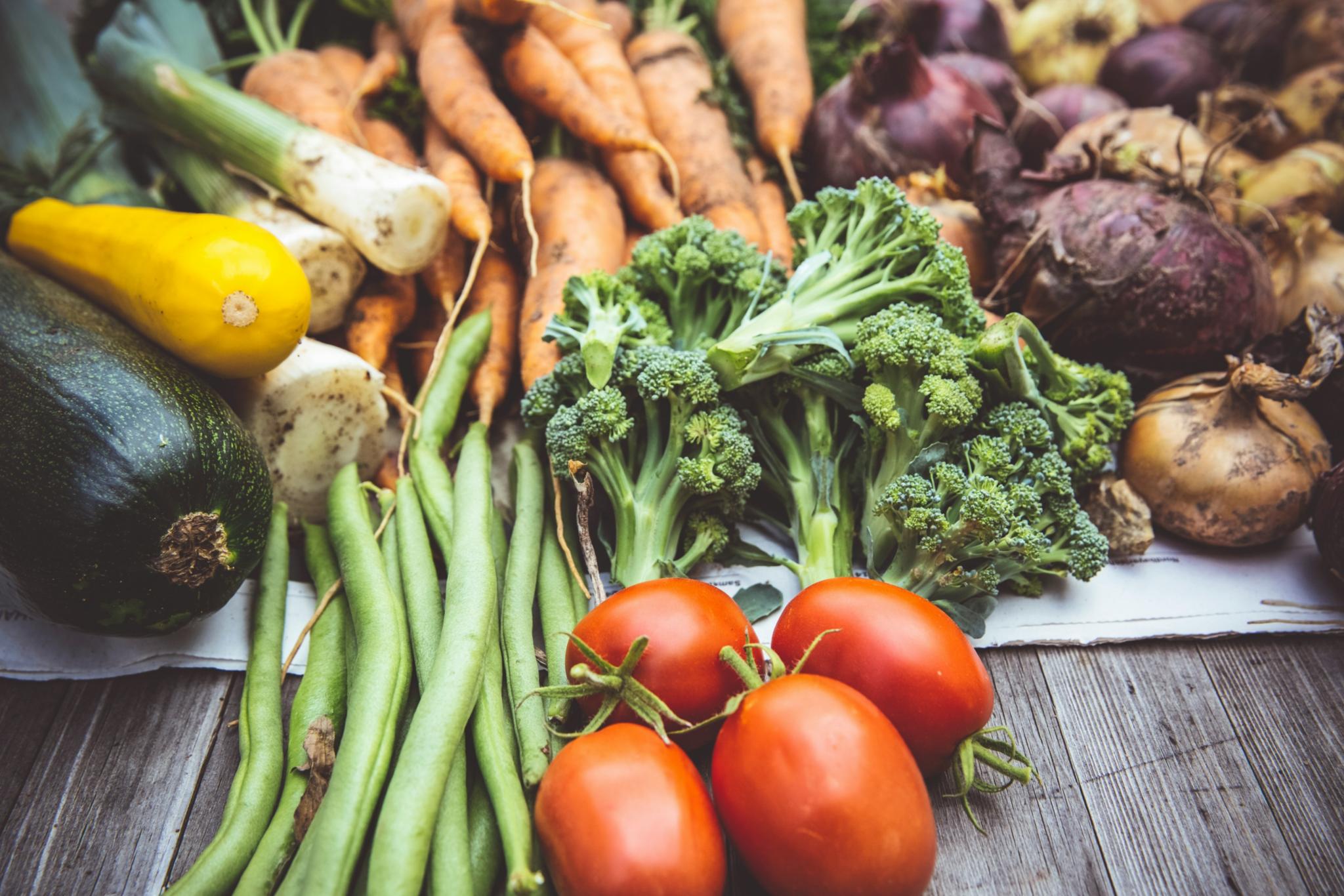 Zucchini, Lauch, Karotten, Zwiebeln, Bohnen, Tomaten und Broccoli liegen auf einem Tisch aus Holz