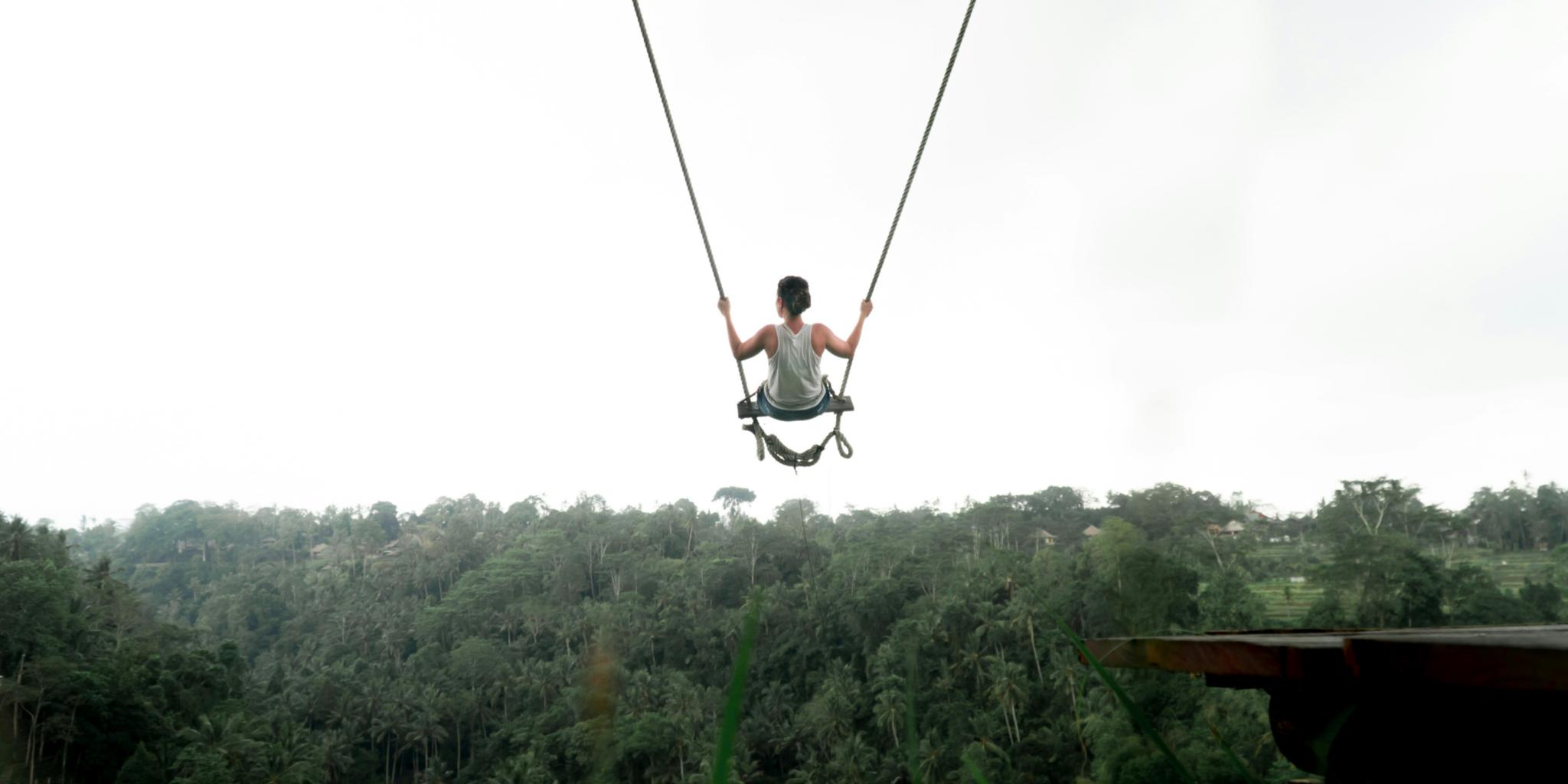 Ein Kind sitzt auf einer sehr hohen Schaukel und schaukelt Richtung Wald